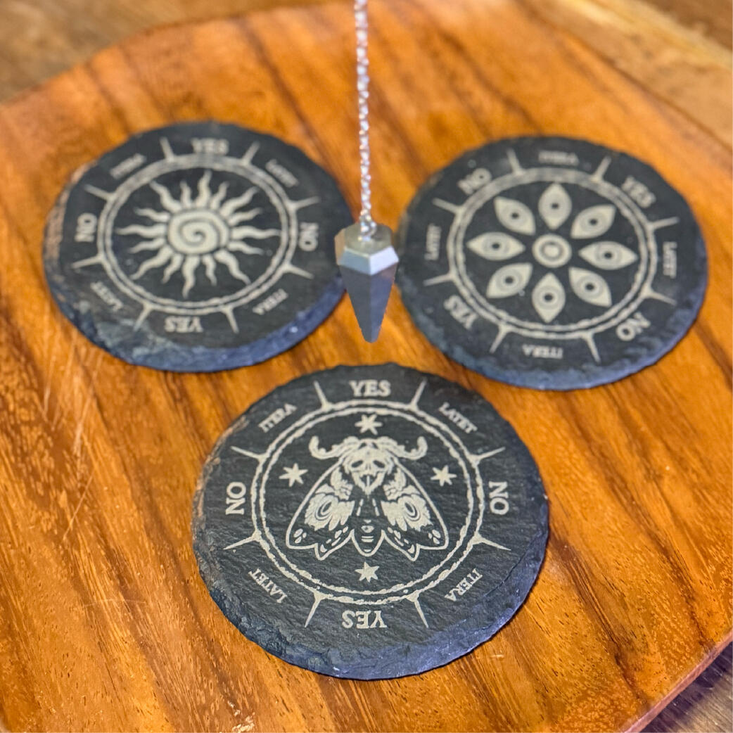 Engraved slate pendulum boards with sun, floral, and moth motifs, a pendulum at rest, Markstones by WMFrewolfe